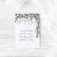 "Now Faith Hope and Love" note card staged on distressed white wood background with eucalyptus leaves and white chiffon at the corner. Artwork features a watercolor wisteria with "now faith hope and love remain, but the greatest of these is love" in calligraphy